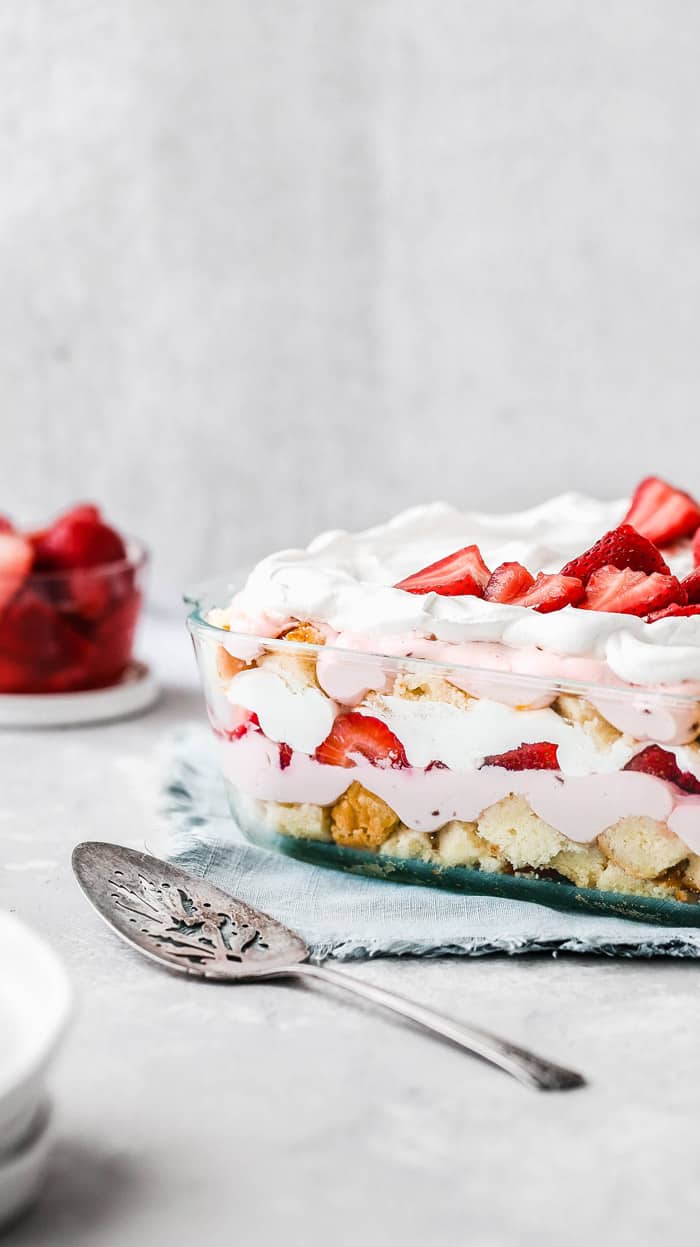 Side view of Strawberry Punch Bowl Cake against white background with bowl of strawberries