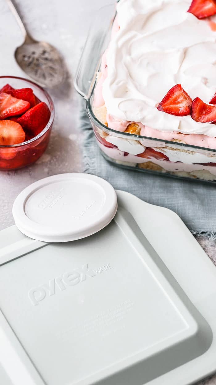 Overhead of cover view of Strawberry Punch Bowl Cake in dish with Pyrex top and bowl of strawberries