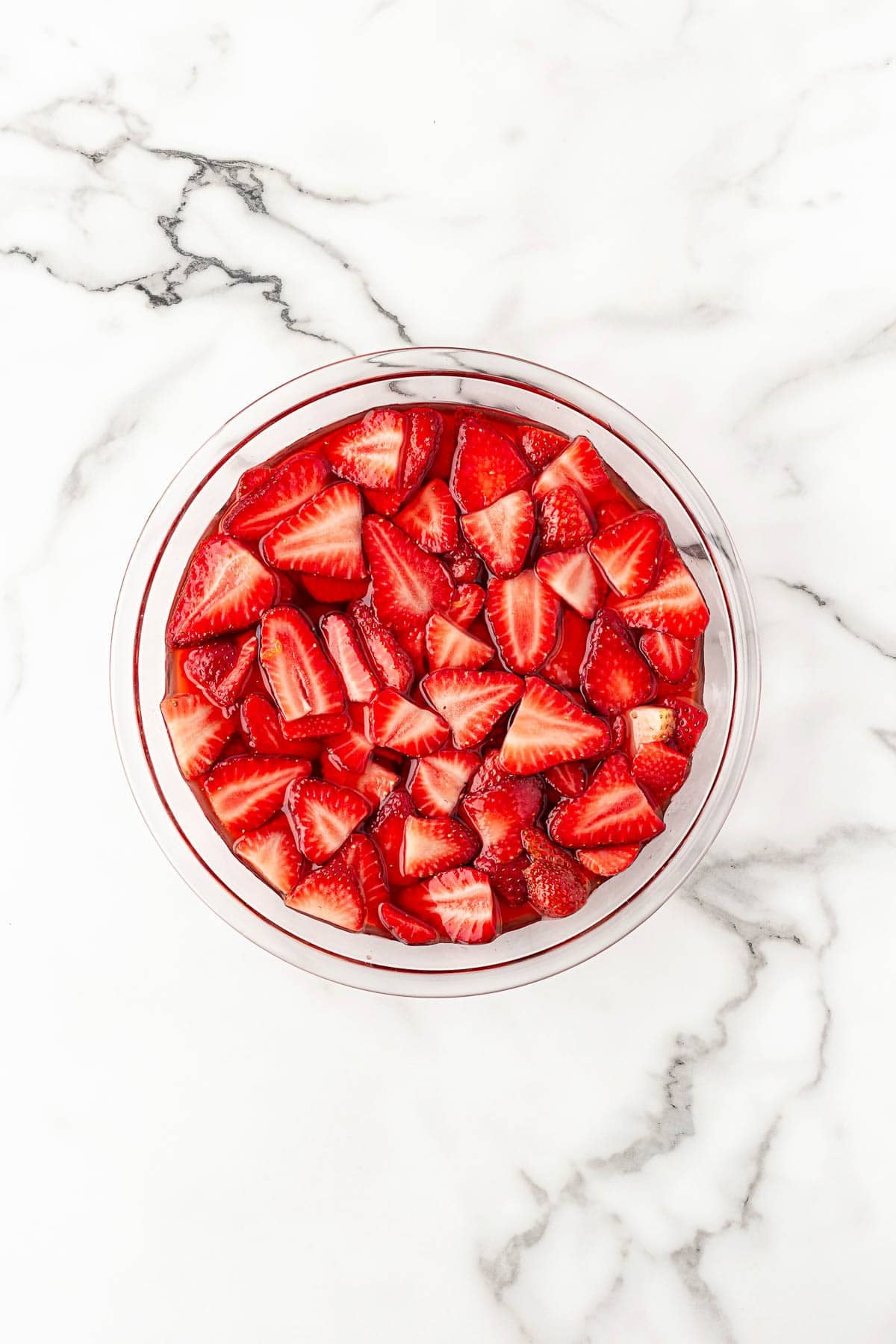 Bowl of sliced strawberries in syrup on a marble countertop