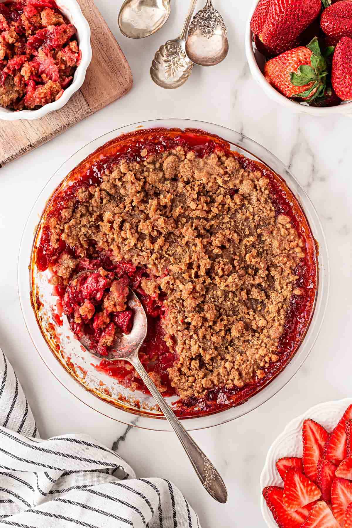 Strawberry crumble in a glass baking dish with a spoon scooping a serving