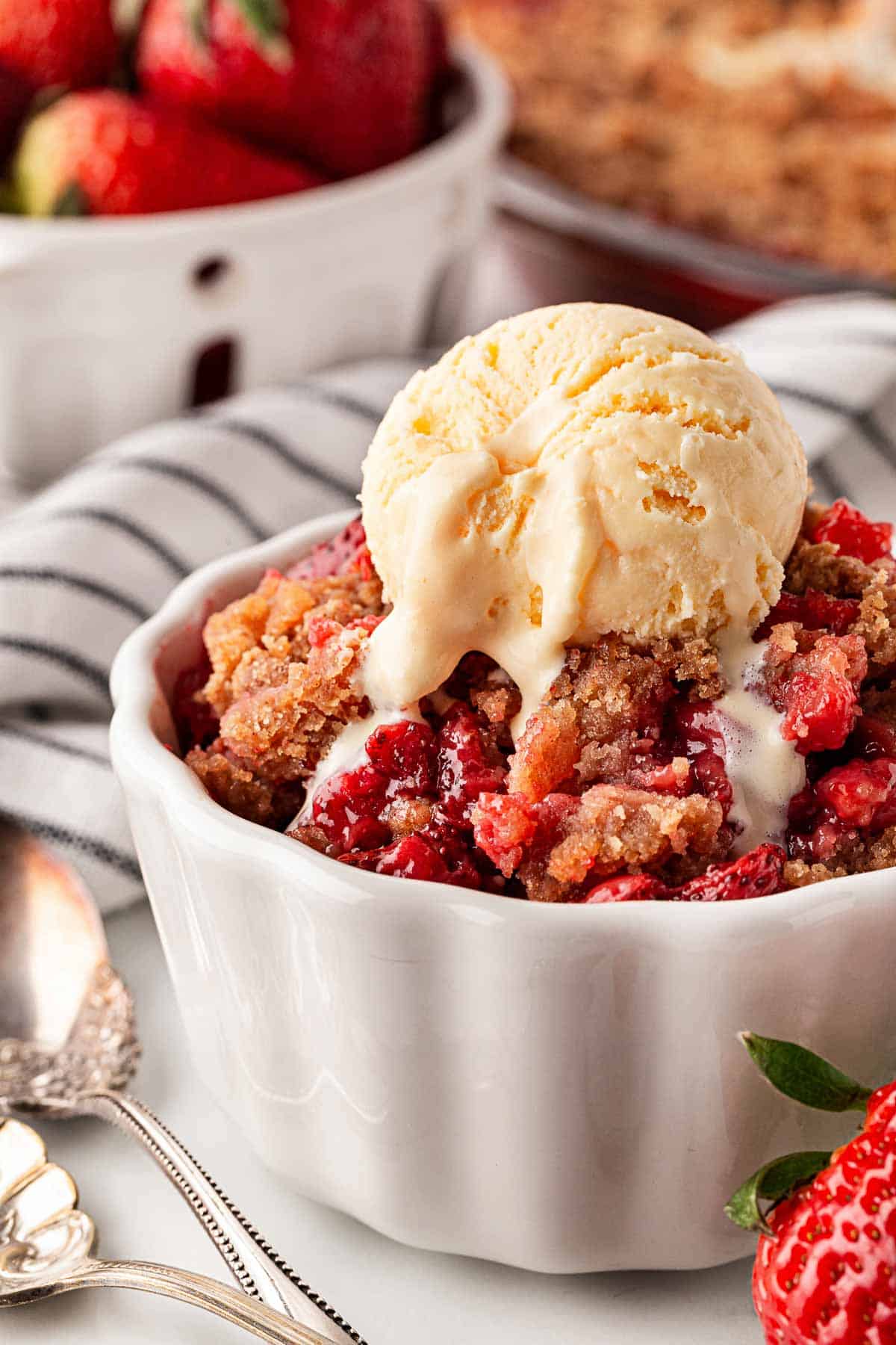 Individual bowl of strawberry crumble with melting vanilla ice cream