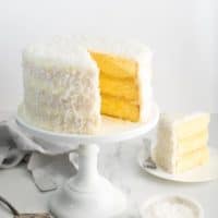 Pineapple Coconut Cake recipe on white cake stand with slice of cake on white plate against white background