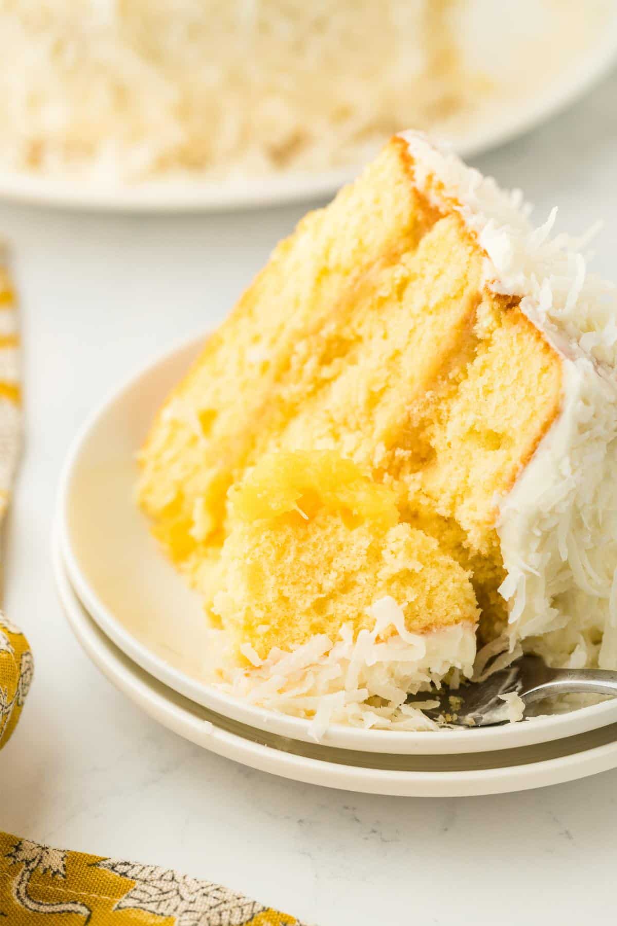 Closeup of a slice of pineapple coconut cake with a bite taken out, showcasing the fluffy, moist interior and coconut topping