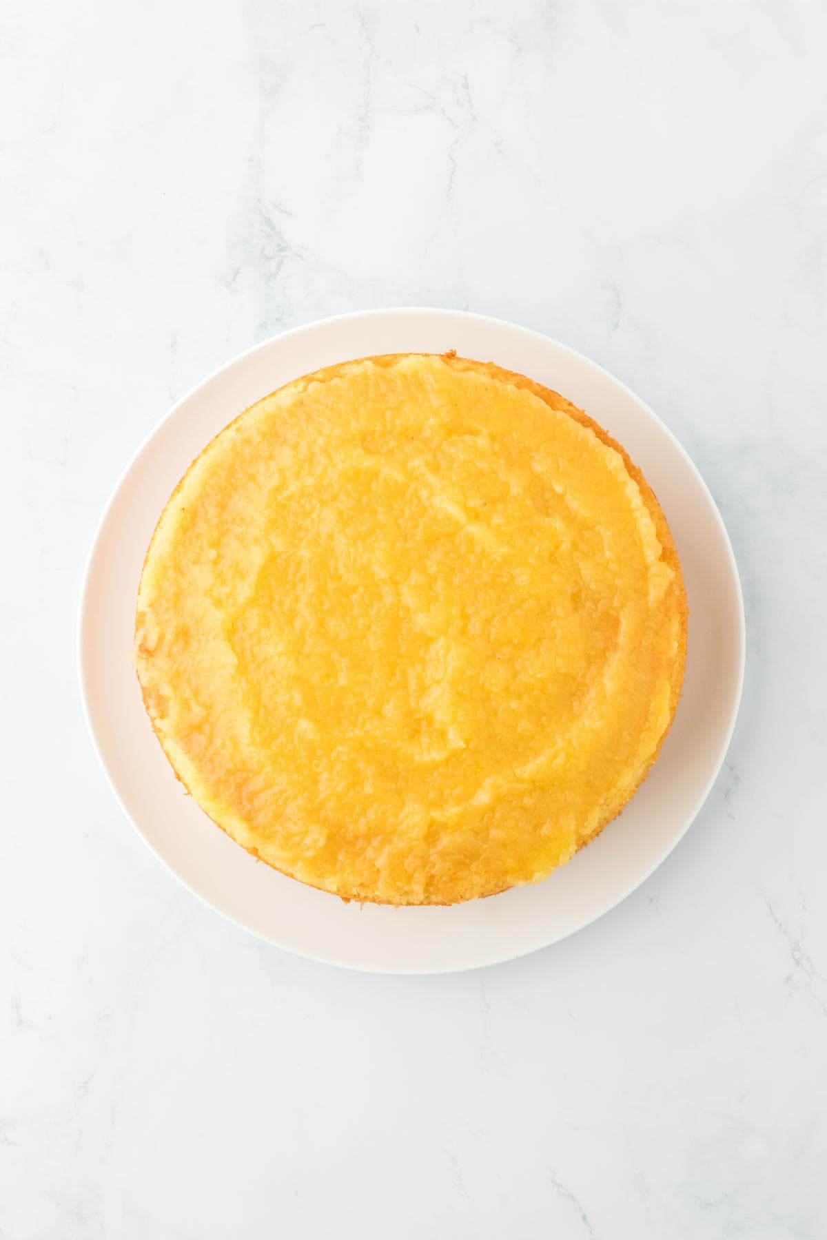 A cake layer completely covered with pineapple filling on a plate