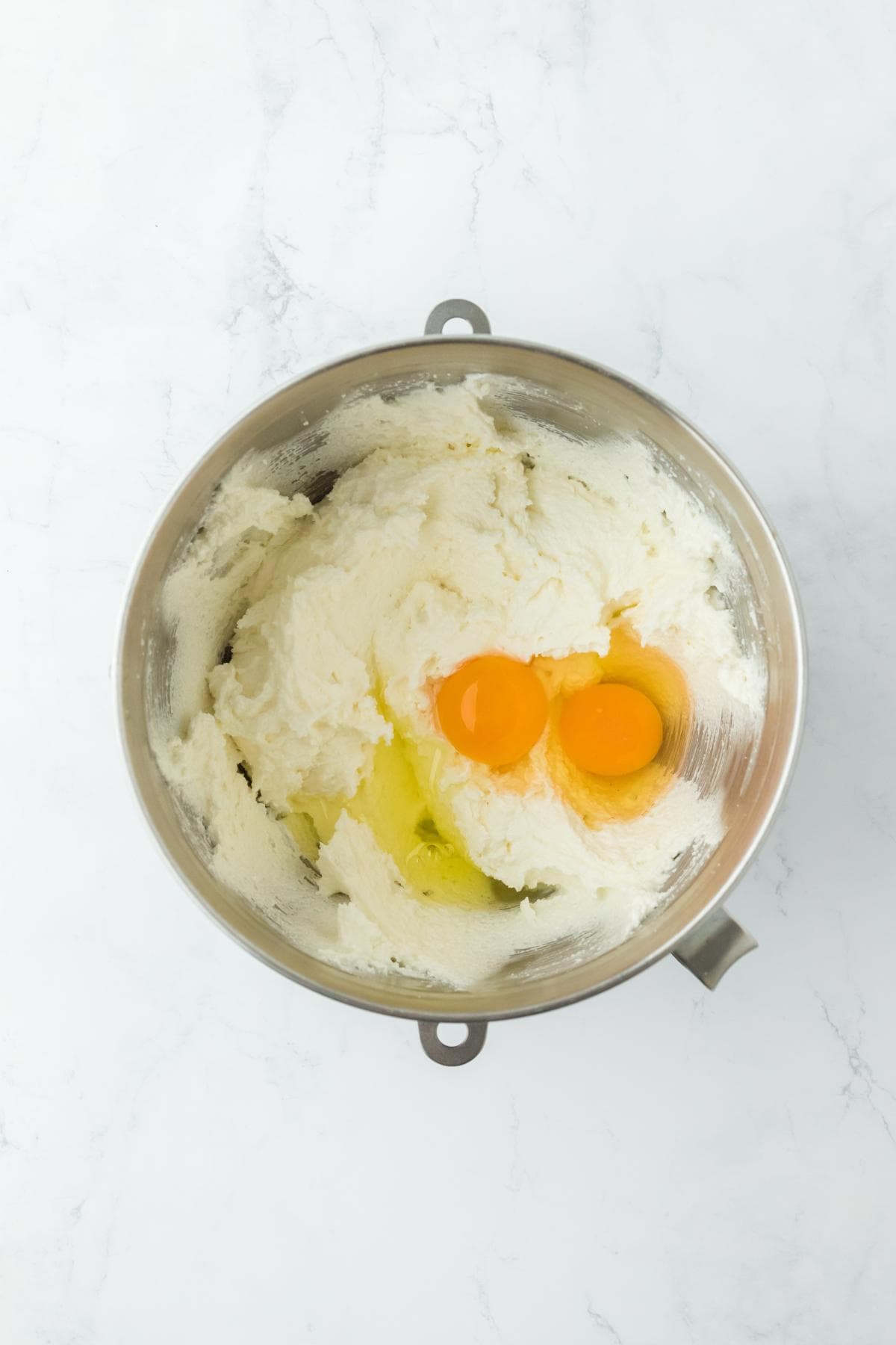 Creamed mixture with two raw egg yolks added on top, in the mixing bowl