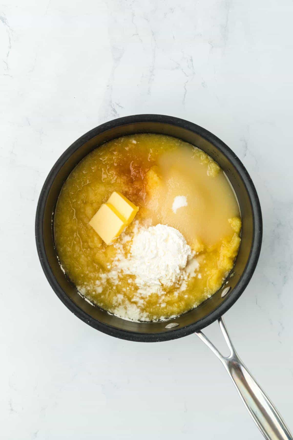 A saucepan containing ingredients like butter, sugar, vanilla extract, juices, and cornstarch, ready for heating