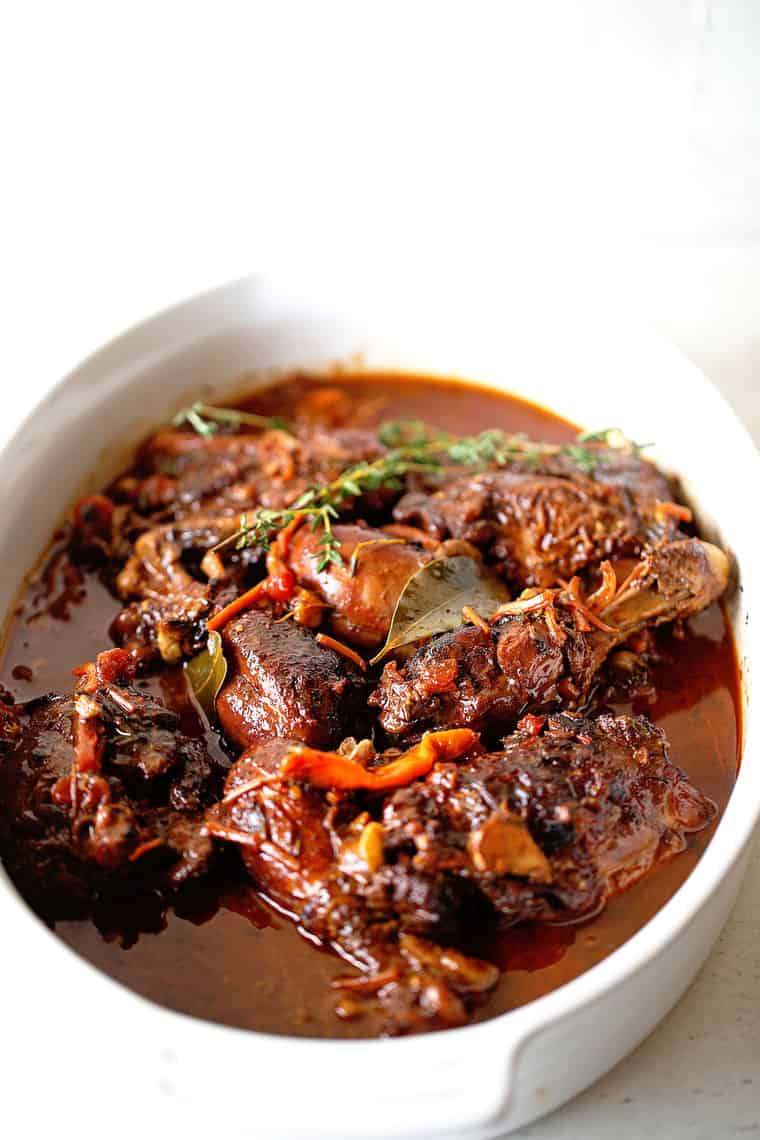 A close up of Brown Stew Chicken recipe in white casserole dish against white background