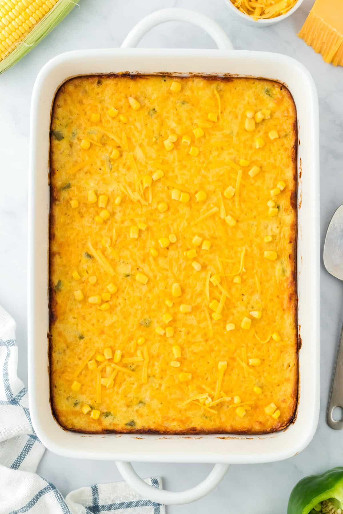 A large white baking dish with simple corn pudding recipe baked on a white background with corn in the background