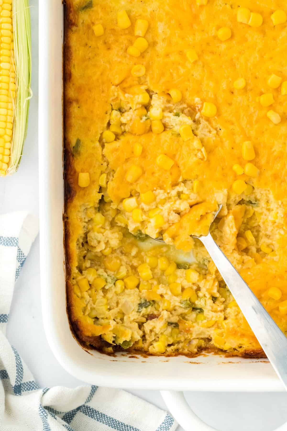 Southern corn pudding on a white background with a large spoon digging into it to serve