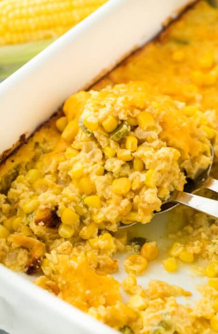 A easy corn pudding spoon going into baking dish on white background