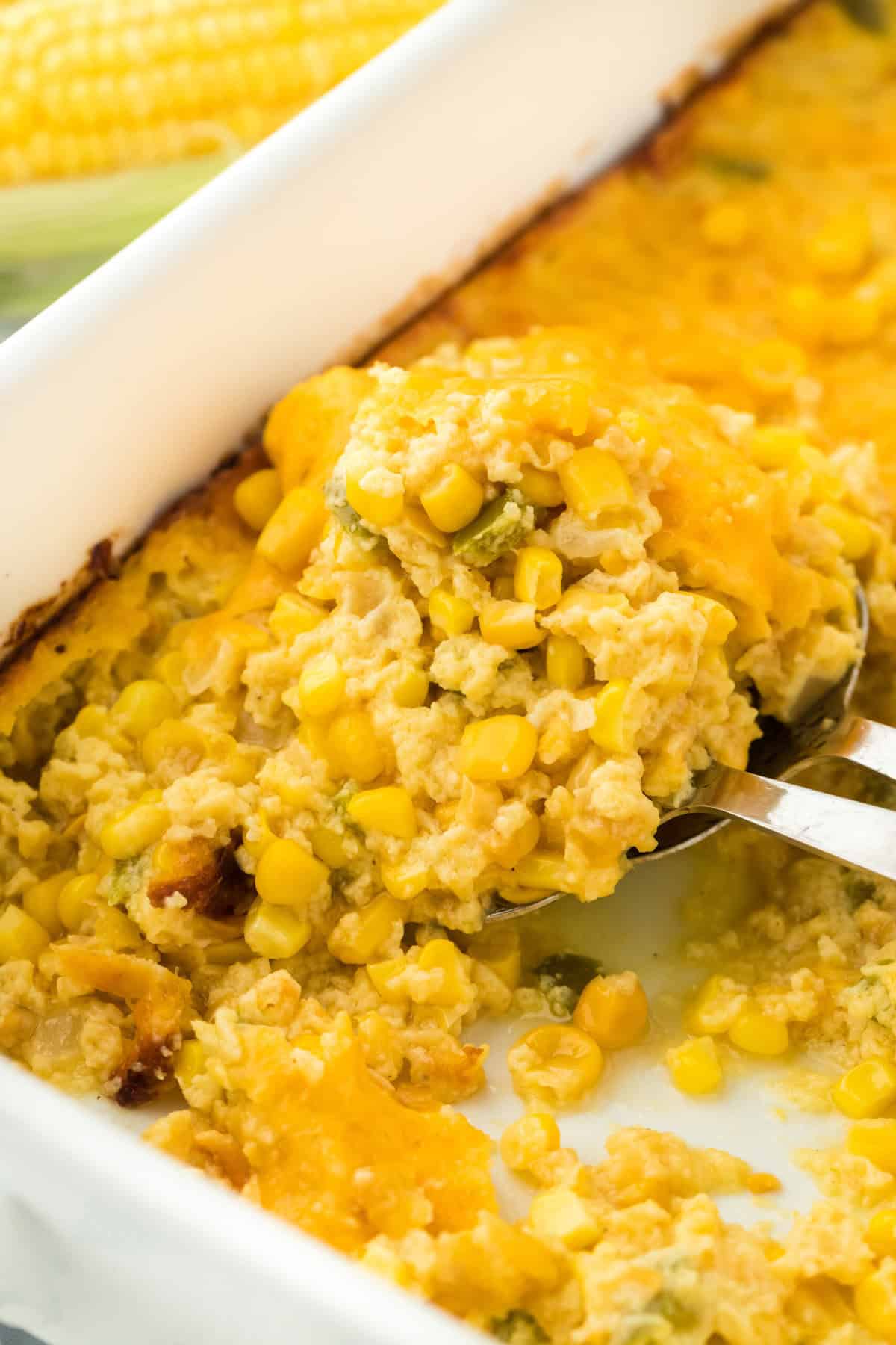 A easy corn pudding spoon going into baking dish on white background