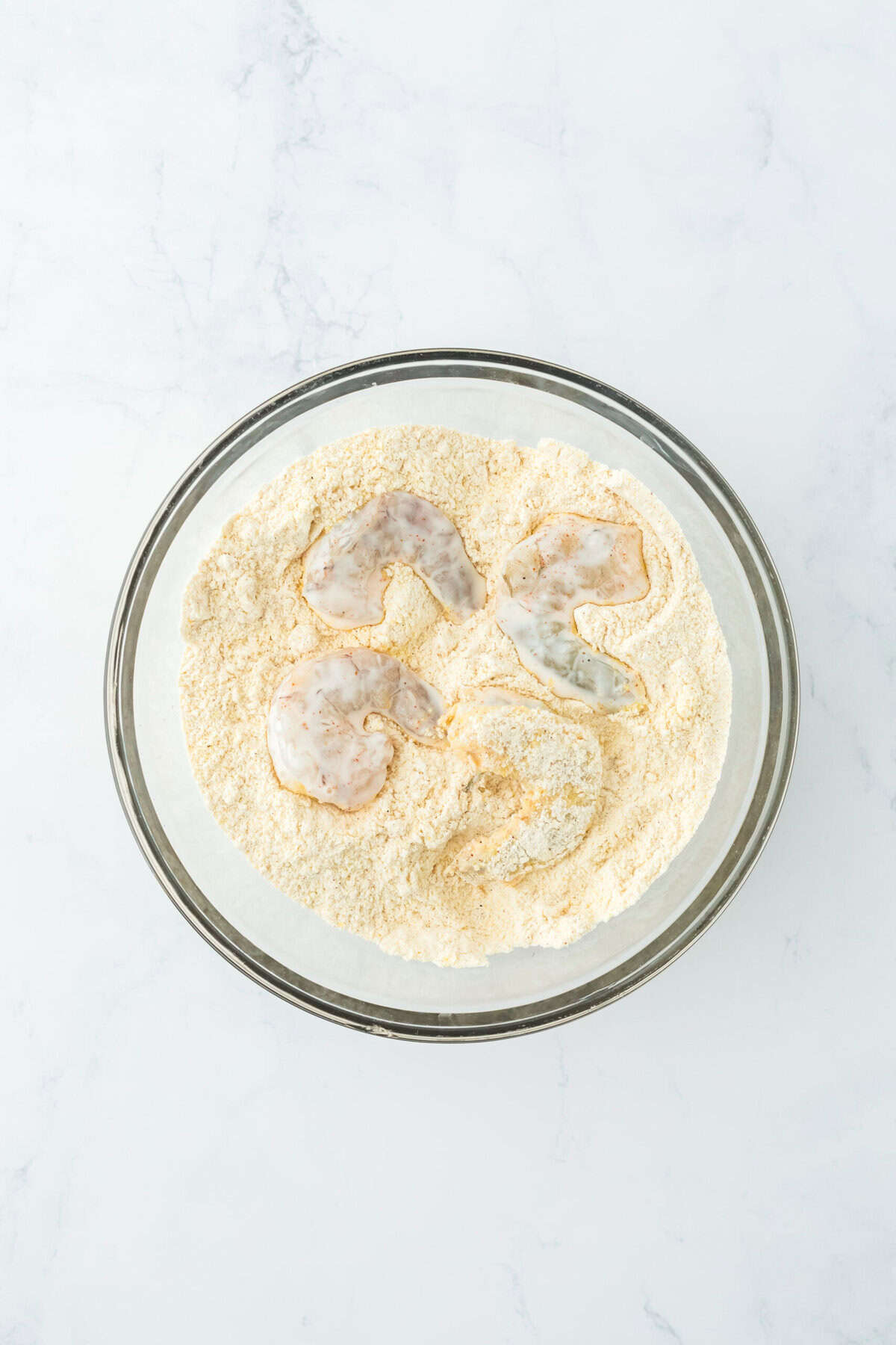 Shrimp added to a cornmeal flour mixture in a glass bowl