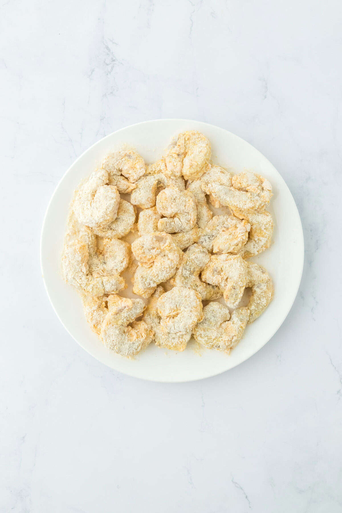 Breaded shrimp on a white plate before frying