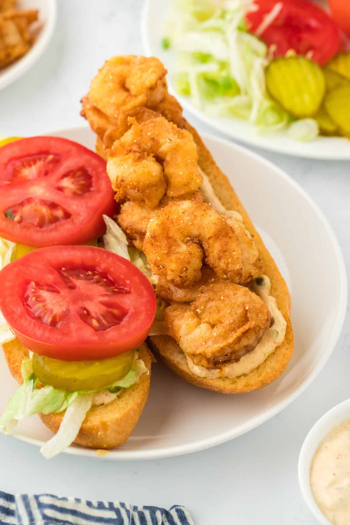 A fried shrimp poboy open faced on a white plate on white countertop ready to serve