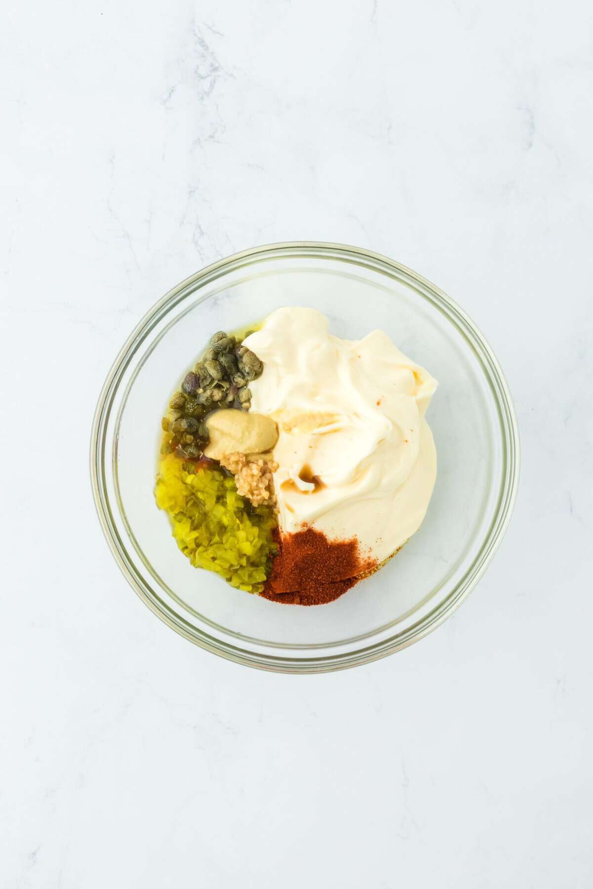 Ingredients in a clear bowl to make remoulade sauce for shrimp poboy recipe on white countertop