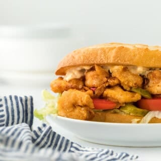 A fried shrimp po boy close up on a white plate ready to enjoy in white background