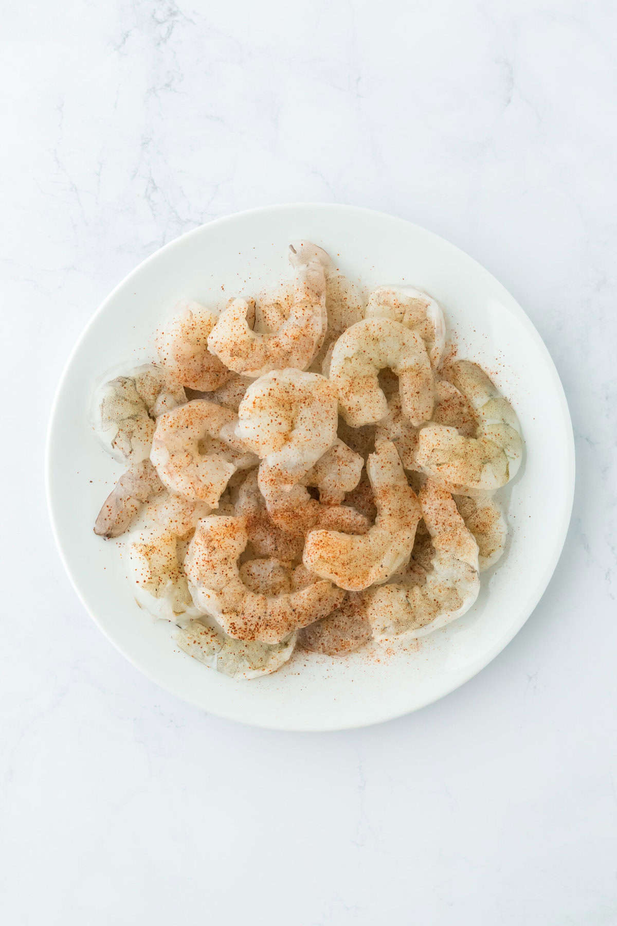 Seasoned shrimp on a white plate on a white countertop