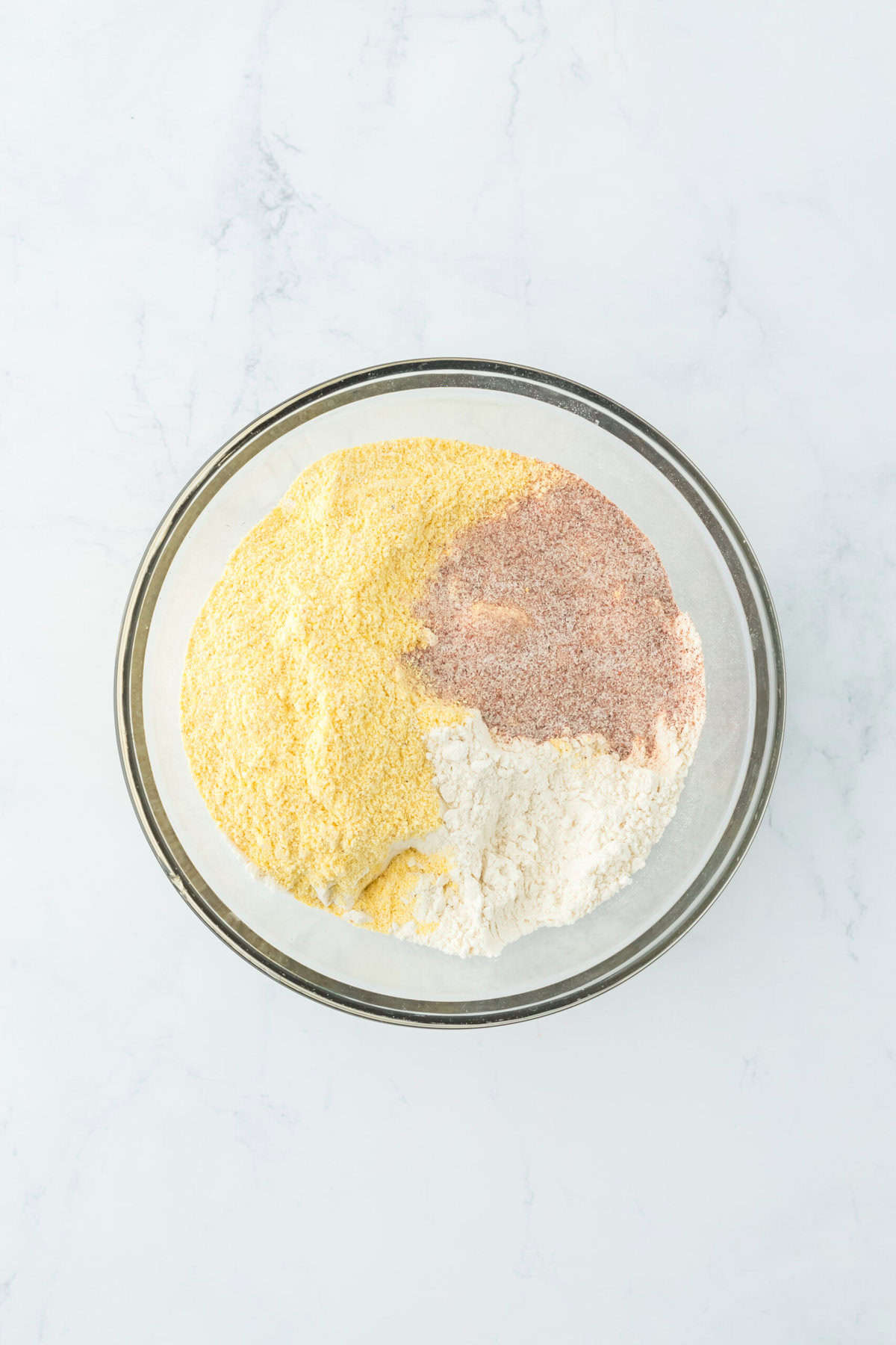 Cornmeal, flour and seasoning mix in a glass bowl on white countertop