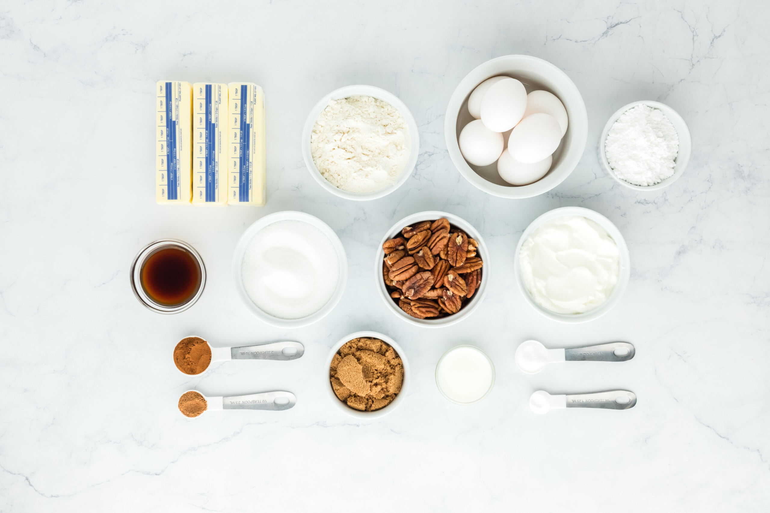 Eggs, pecans, butter, vanilla, flour, sugar and other ingredients in white bowls on a white background for baking