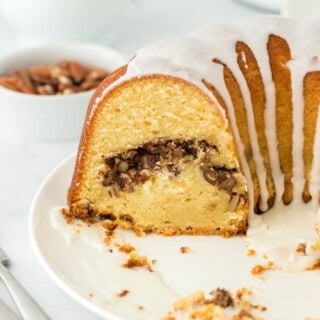 A homemade sock it to me cake cut open on a white plate with pecans in a white bowl with white background