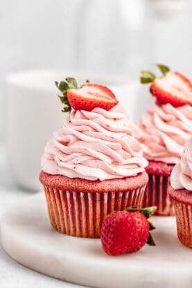 A close up of cupcakes with strawberry buttercream with half berries on top