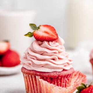 One cupcake with strawberry buttercream with wrapper coming off