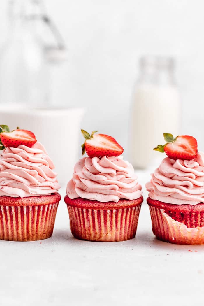 Three strawberry cupcakes lined up next to each other with strawberry buttercream