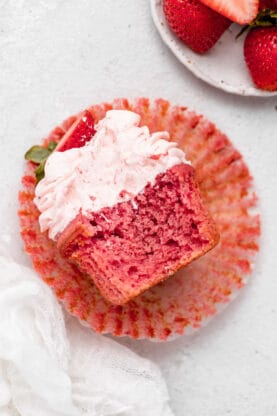 A bite taken out of strawberry cupcake on wrapper