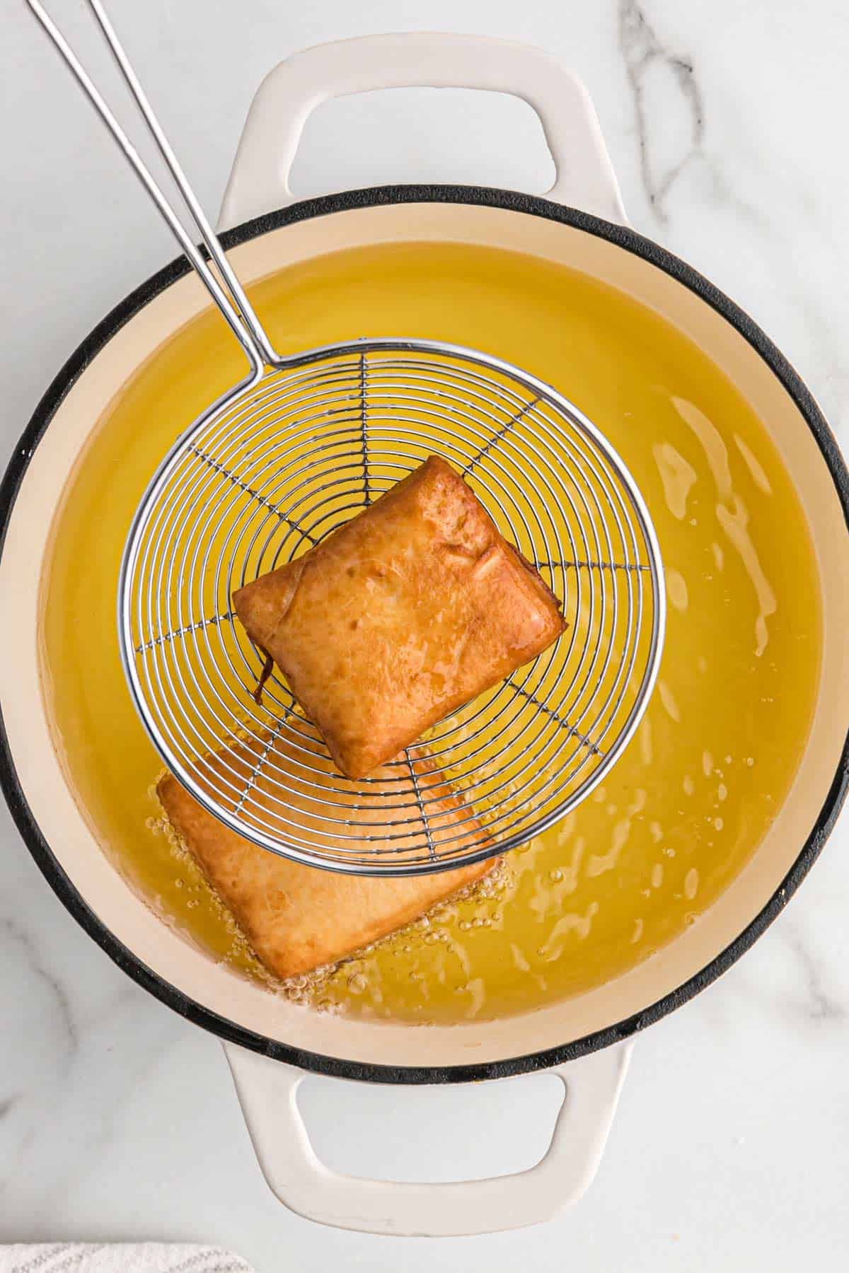 Scooping out a golden brown beignets from the pot.