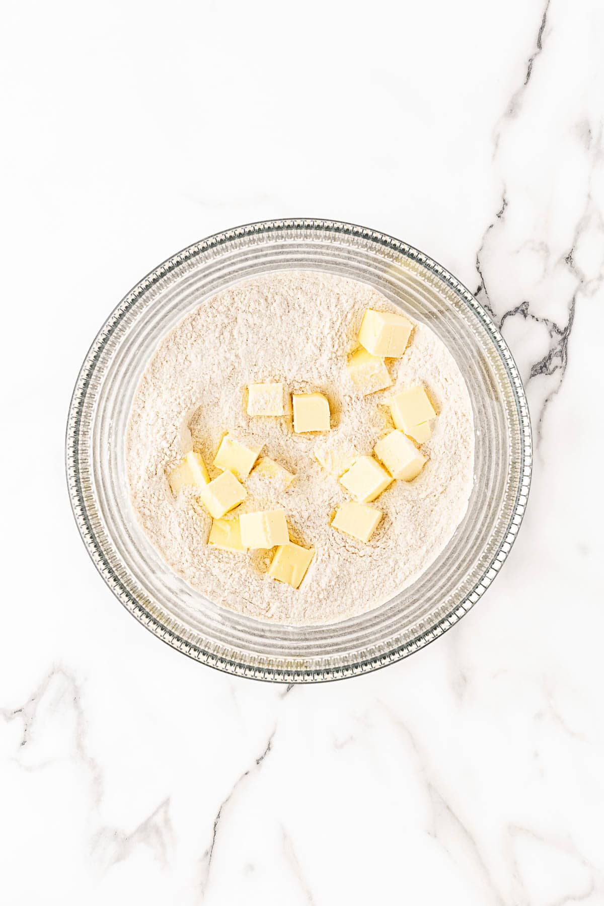 Cubed butter added to flour mixture in glass bowl