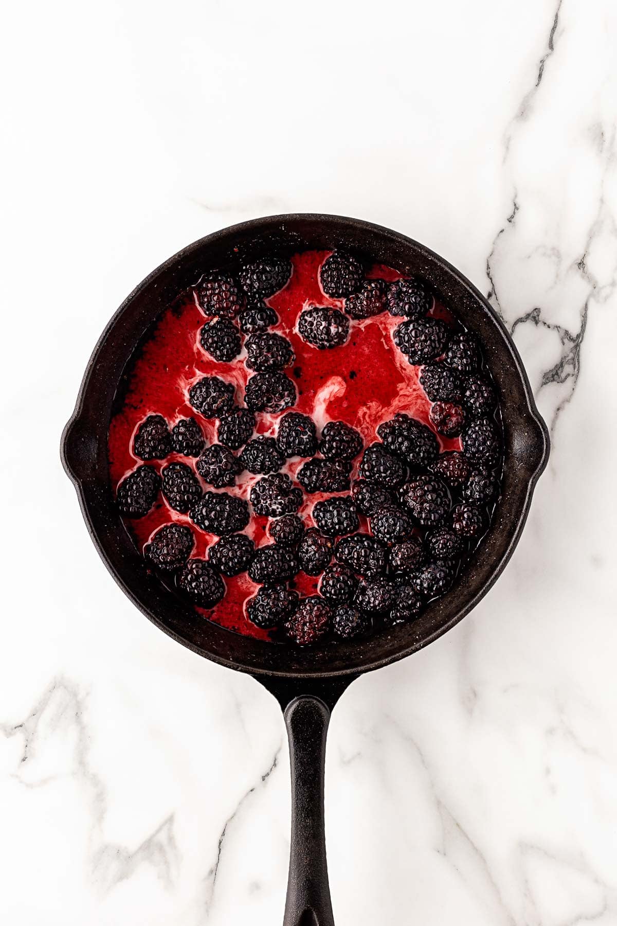 Fresh blackberries in bright red cobbler filling in skillet