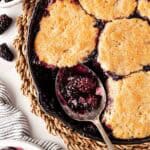Overhead shot of spoon scooping warm blackberry cobbler from skillet