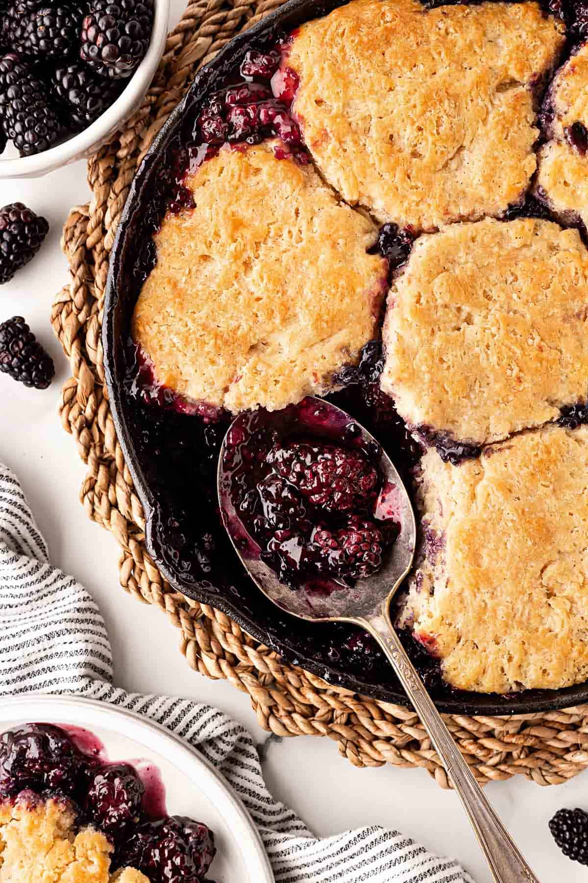 Overhead shot of spoon scooping warm blackberry cobbler from skillet