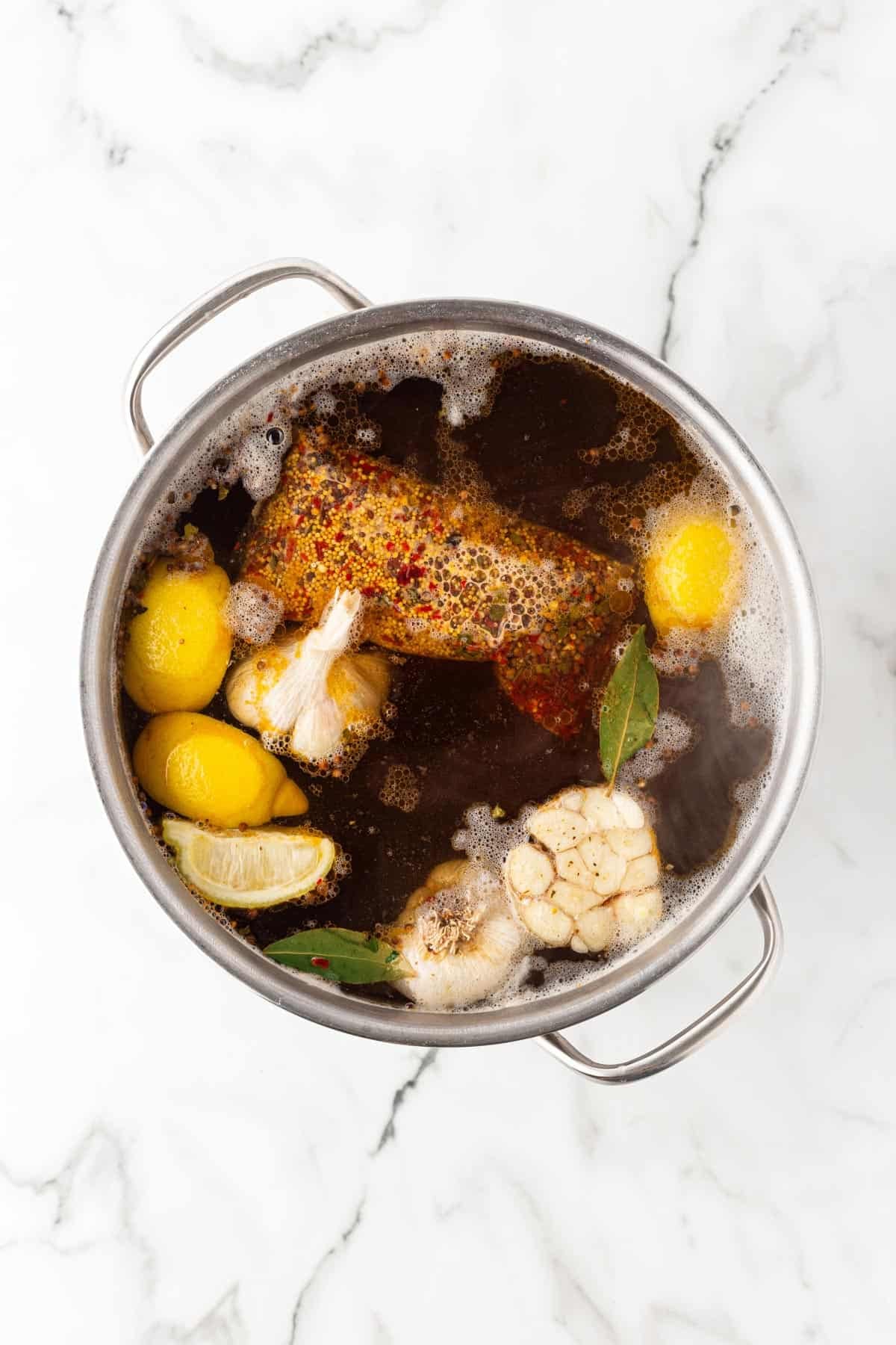 Pot of low country boil broth with lemons, garlic, bay leaves, and seasoning before cooking