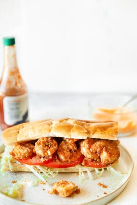 Shrimp po'boy on plate with hot sauce and remoulade sauce against white background