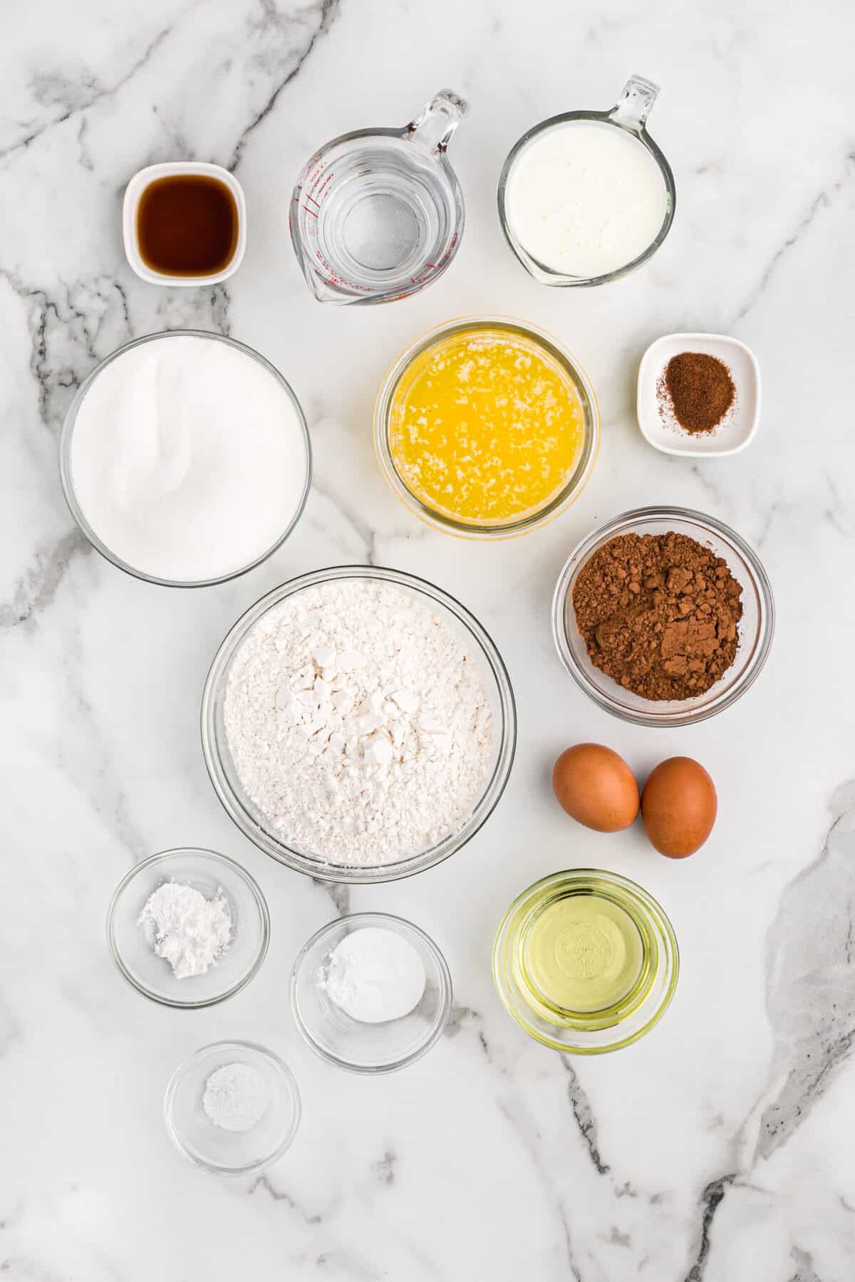 Ingredients in white bowls to make a chocolate layer cake for a birthday on white countertop