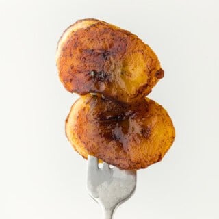 Two fried sweet plantains on a silver fork against a white background