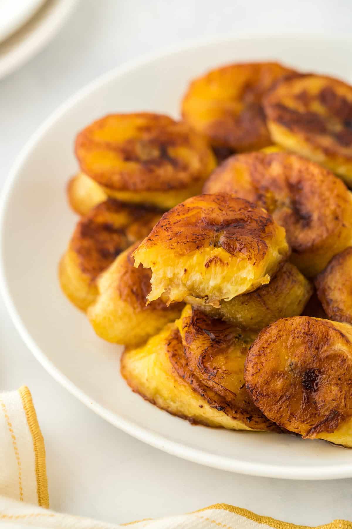Slices of sweet fried plantains on a white plate with one bitten into