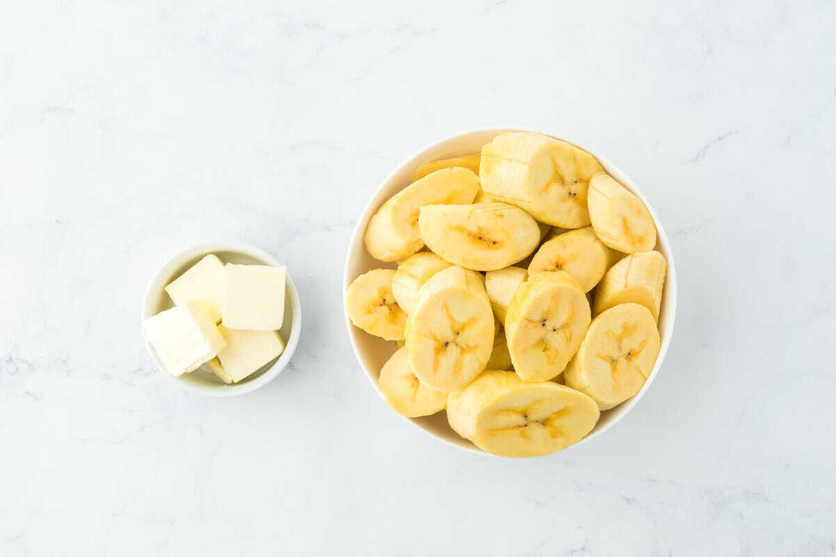 Plantain slices in a white bowl with butter cubes on a white background