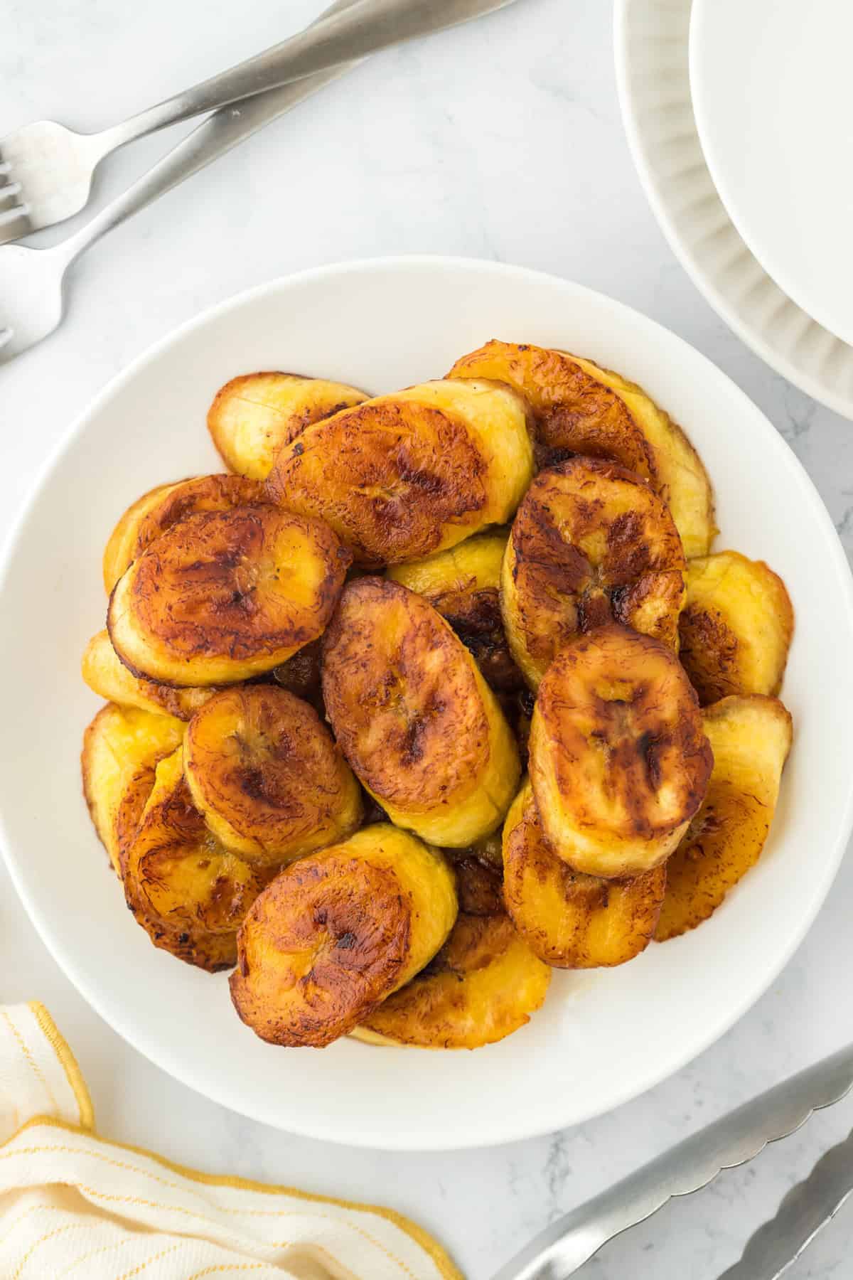 A white plate against a white background with slices of fried sweet plantains