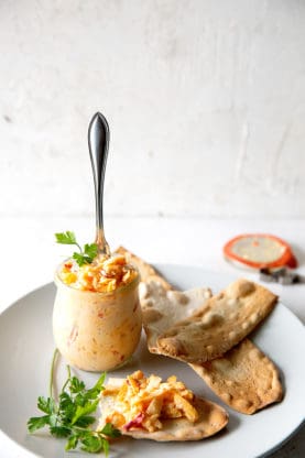Southern Pimento Cheese spread in a glass bowl with spoon over white plate with crackers