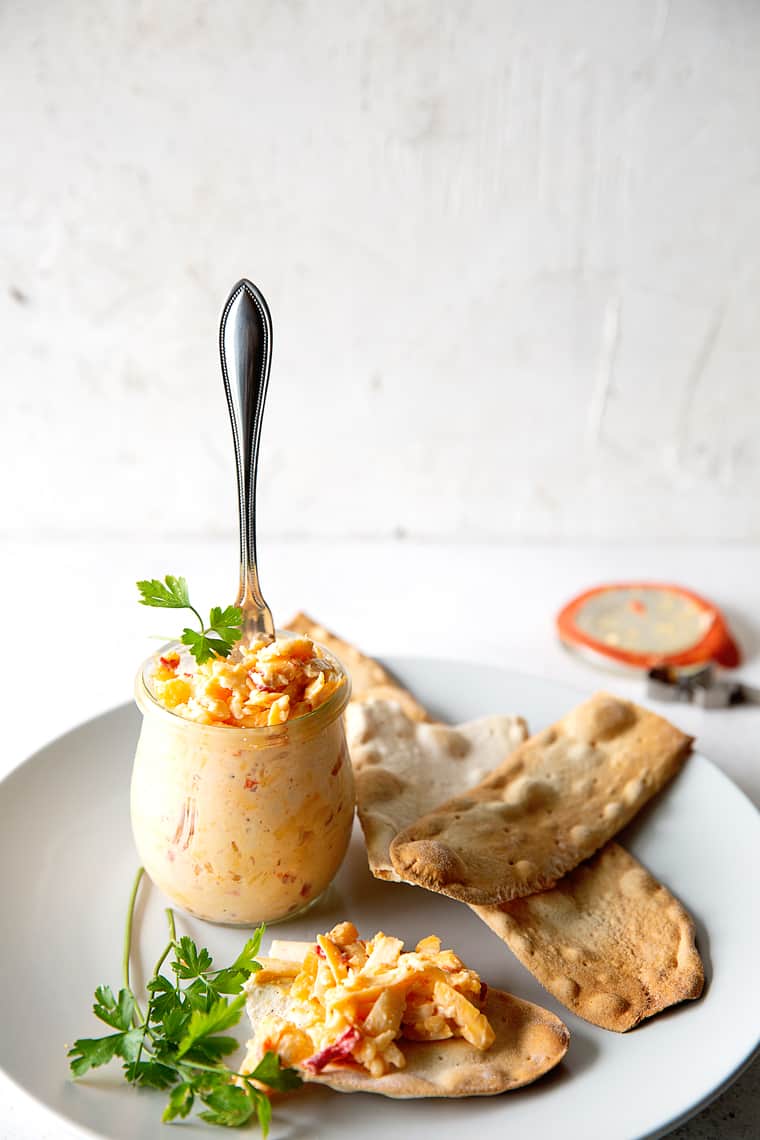 Southern Pimento Cheese spread in a glass bowl with spoon over white plate with crackers