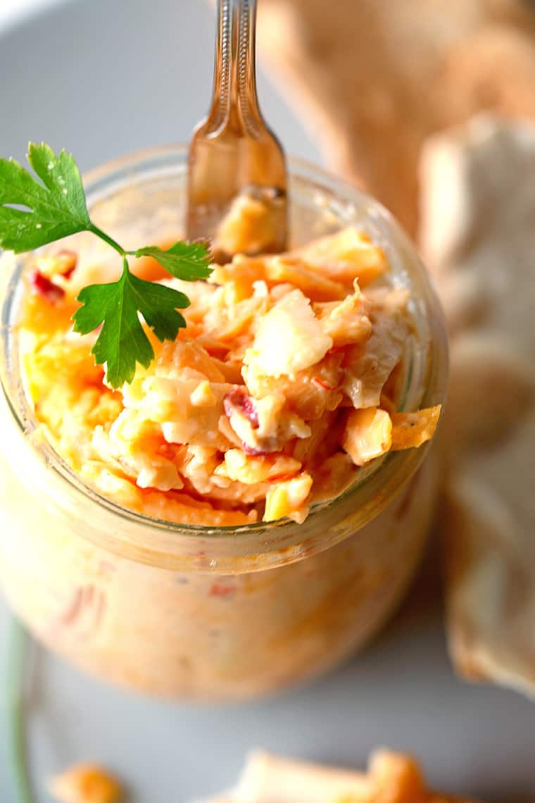 Close up overhead of pimento cheese recipe in white jar with parsley garnish