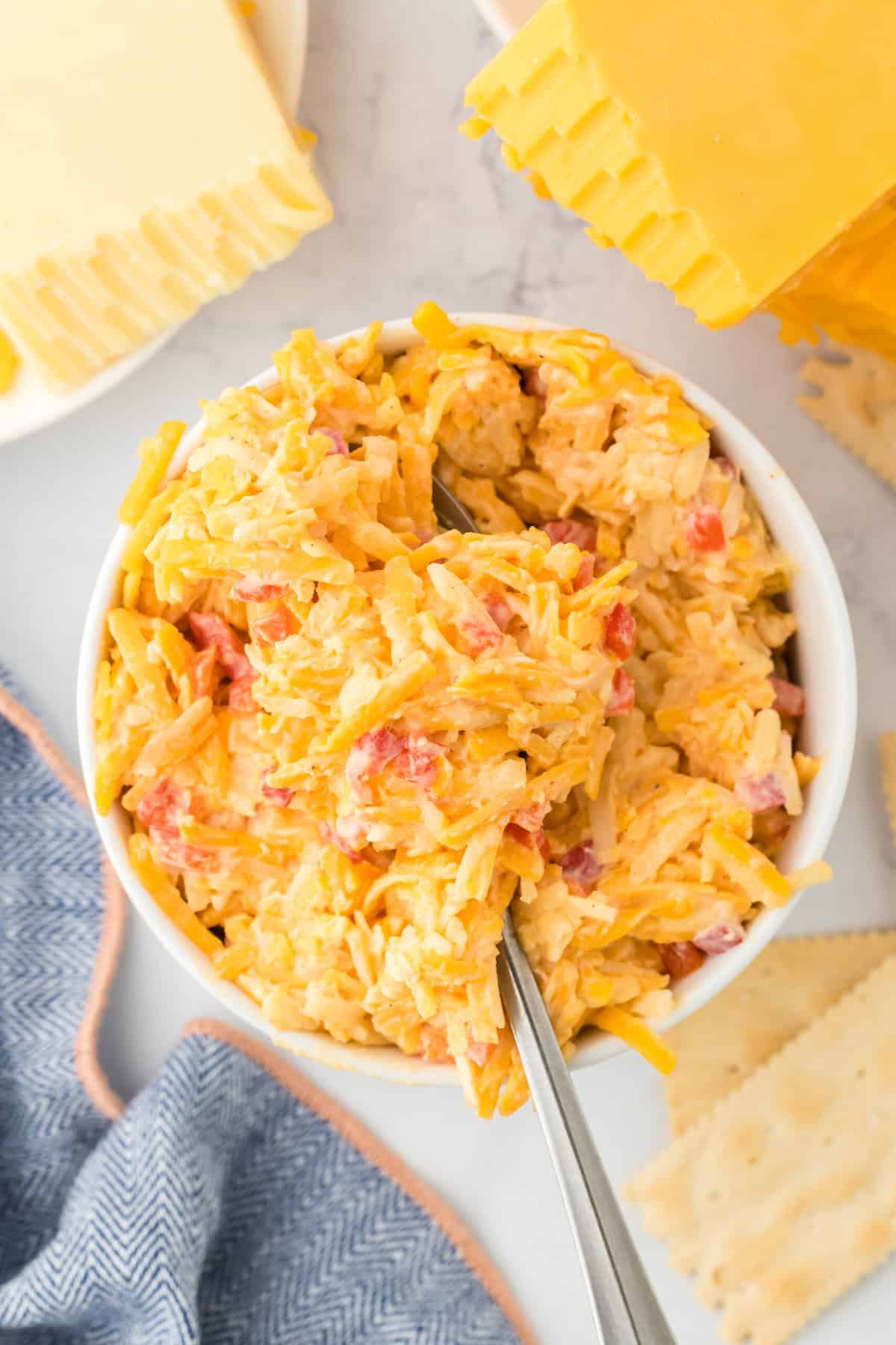 A homemade pimento cheese spread in a white bowl with a spoon inside