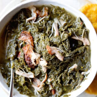 A close up of a white bowl filled with mustard greens with smoked turkey with hot water cornbread