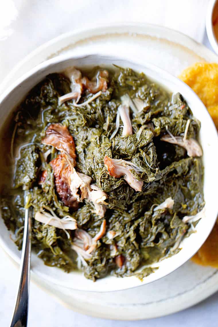 A close up of a white bowl filled with mustard greens with smoked turkey with hot water cornbread
