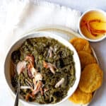 A white bowl with mustard greens and cornbread over a white napkin