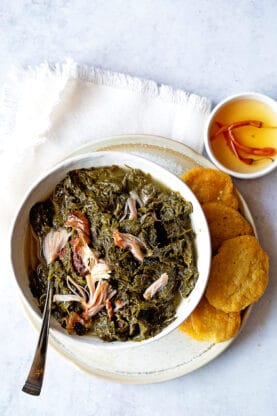A white bowl with mustard greens and cornbread over a white napkin