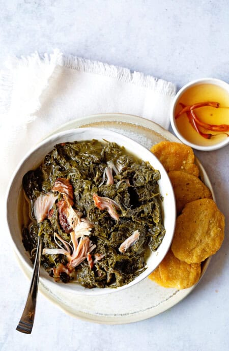 A white bowl with mustard greens and cornbread over a white napkin