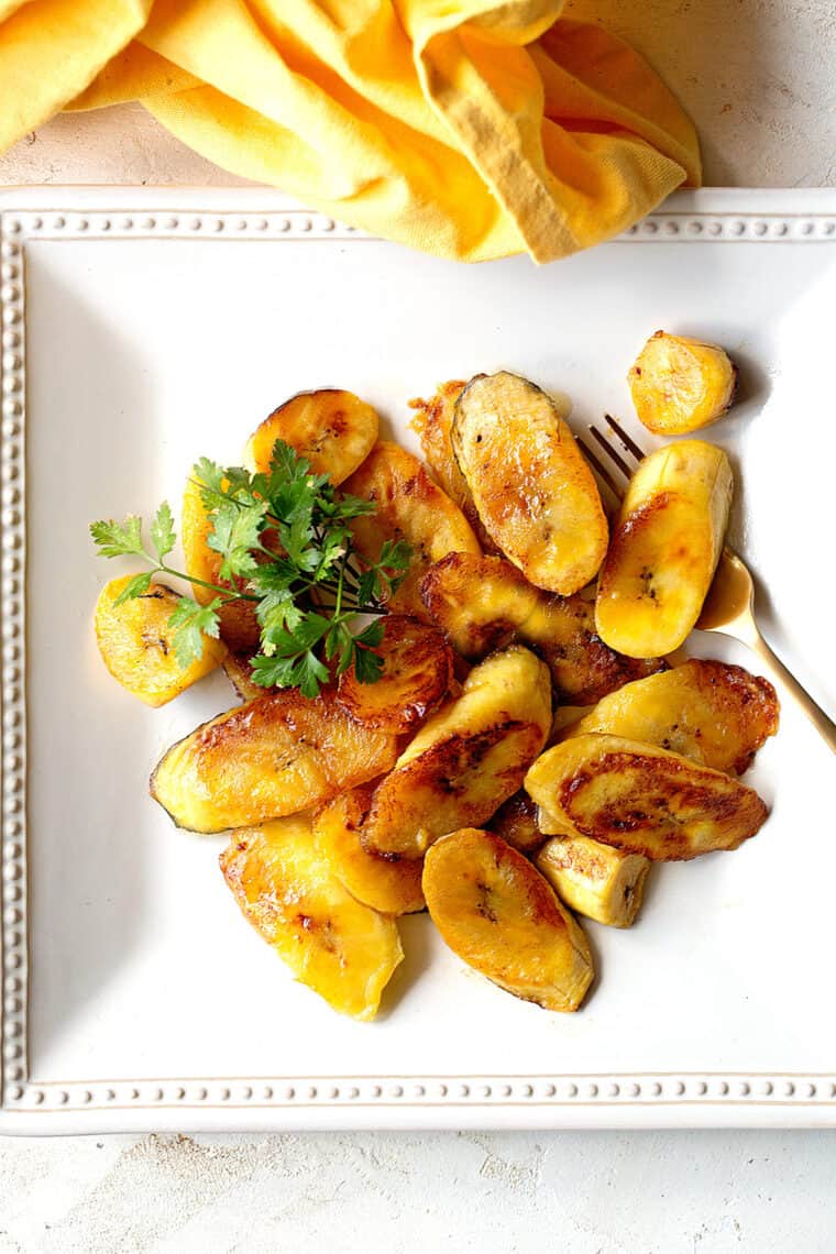 Overhead of white plate with fried sweet plantains with yellow napkin